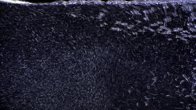 Clear drinkable natural mineral water pouring into a glass. Extreme macro close-up of carbonated H2O filling full screen on clean black background. Refreshing stream of rising pure clean bubbly liquid