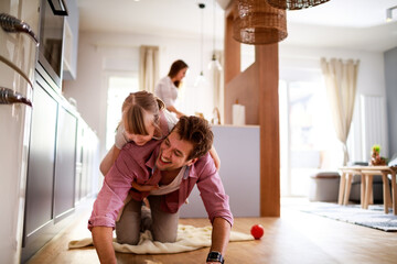 Smiling father giving piggyback ride to little daughter on living room floor