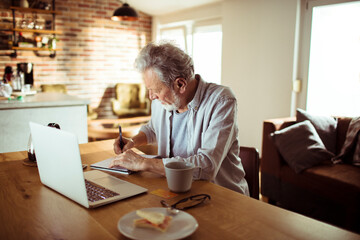 Senior man working from home and taking notes