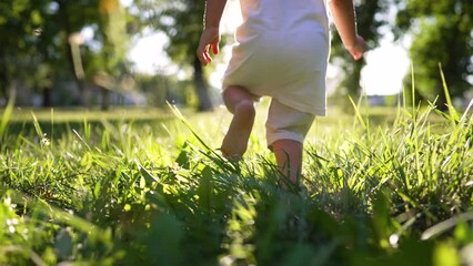 Boy kid run on grass in summer in park. Feet close up on green grass in sun. Kid dream in nature. Children play in the park on vacation. Active child jogging on a picnic in summer in a park in nature - Powered by Adobe