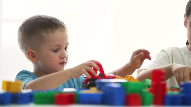 Teamwork of children in kindergarten. Brother and sister play blocks at table in colored toys. Preschool education in kindergarten. Children play with toys. Home games in the family. Home kindergarten