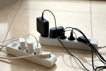 Overloaded power boards. Power strips with different electrical plugs on white floor. Concept of...