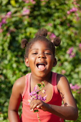 happy small african girl with a joyful face holding some flowers outdoors