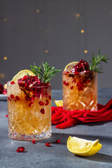 two glasses with cocktails made of ice, lemon juice, alcohol and pomegranate juice. Cocktails are decorated with pomegranate seeds, fresh rosemary and lemon. dark gray background. Night life. 