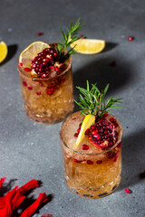 two glasses with cocktails made of ice, lemon juice, alcohol and pomegranate juice. Cocktails are decorated with pomegranate seeds, fresh rosemary and lemon. dark gray background. Night life. 