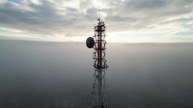 tall communications tower high in the sky and the clouds, dense fog around on a beautiful sunny morning, camera on drone circling around the tower showing the antennas and aerials