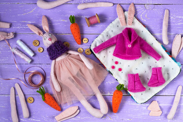 Pink rabbit doll girl and body preparations (dolls blanks) hands and legs for textile toys and doll. Sewing supplies and accessories on purple wooden background. Sewing textile dolls. Top view