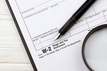 IRS Form W-2 Wage and Tax Statement blank on A4 tablet lies on office table with pen and magnifying...
