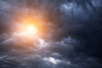 Epic dramatic storm sky with sun. Dark grey blue cumulus rain clouds with orange yellow light and...