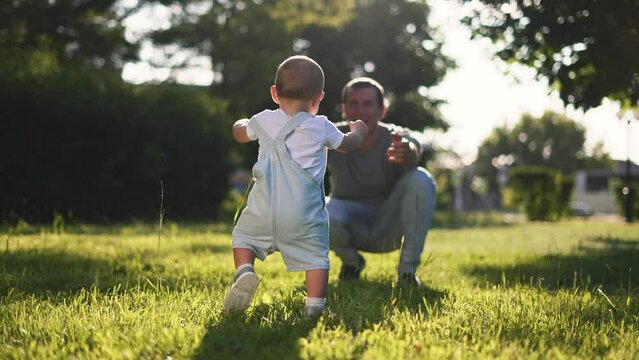Happy family. Baby takes first steps with his parents.First steps on picnic in park on green grass,baby plays with his mother and father.Fun in summer in park on grass.First steps in spring happy days