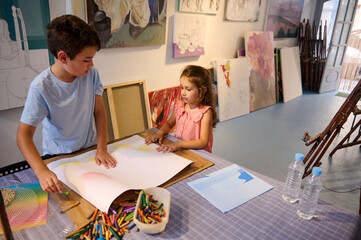Obraz premium Adorable kids, a teenage boy and preschool girl drawing on white paper sheet during art class. People. Kids and hobbies