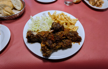 plate with pieces of roast goat meat with French fries and cut lettuce