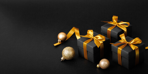 Black gift box with golden ribbon bow on black background