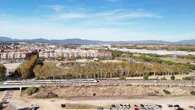 Trenes Renfe R2 Rodalies entrando y saliendo de la estaci&oacute;n de Santa Perp&egrave;tua de Mogoda, con vistas a Montserrat y al lago de Parc Central y un partido de f&uacute;tbol, grabado desde dron 4k 60fps.