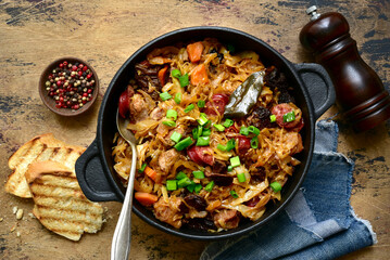 Bigos - traditional dish of polish cuisine,stewed cabbage with meat, sausage and dried mushrooms in a pan . Top view with copy space. - obrazy, fototapety, plakaty