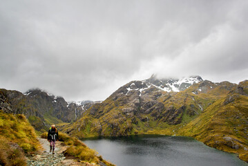 View of the lake harris with snowy mountains and a hiker at the summit of the Routeburn, New Zealand