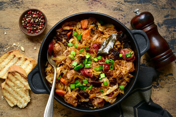 Bigos - traditional dish of polish cuisine,stewed cabbage with meat, sausage and dried mushrooms in a pan . Top view with copy space. - obrazy, fototapety, plakaty