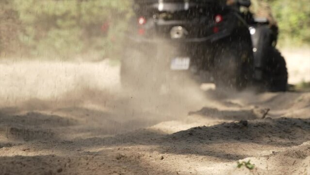 A quad bike spinning its wheels on sand, kicking up dust into the air