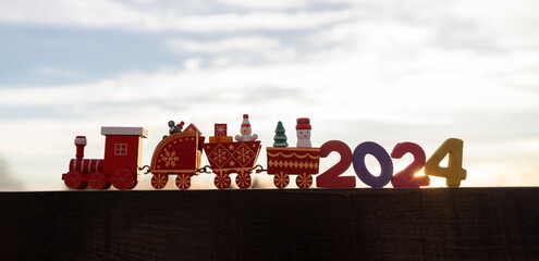 children's wooden festive red toy train and numbers 2024 against the background of the sky and the setting sun. festive mood. Time to make wishes, bright future. Happy New Year and Merry Christmas. - obrazy, fototapety, plakaty