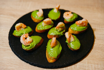 Bruschetta with avocado puree and shrimp on a black slate board, appetizer presentation