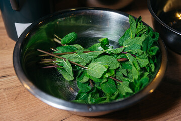 A metal bowl filled with green mint leaves soaked in water on top of a wooden table