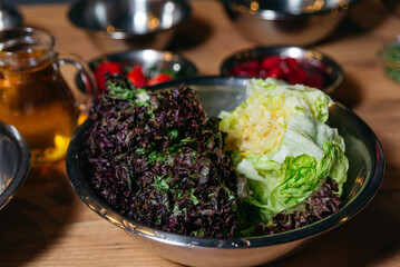 Washed leaves of fresh iceberg lettuce and juicy purple curly lettuce, close-up, in a stainless steel bowl