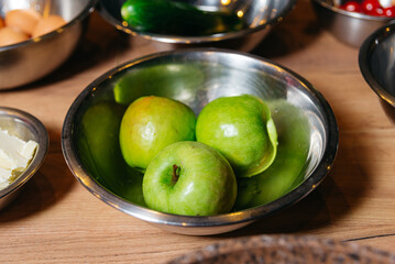 A wooden table topped with metal bowls filled with apples