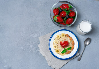 Oatmeal with banana slices, almonds and strawberries. Oatmeal with fruit and milk. Healthy breakfast. Healthy eating. View from above.