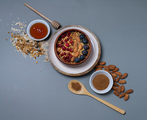 Granola in a wooden bowl on a white plate with cranberries and nuts on a gray background. Healthy...