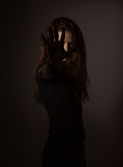 Beauty young witch with long dark hair conjures the hand covering the face on studio dark...
