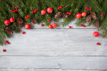 Christmas wooden background with fir branches, red apples, berries, cones. Space for copy, congratulations text.