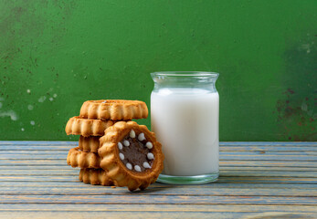 Milk in a glass container with biscuits on a wooden table.