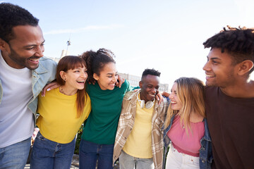 Multiracial young people team hugging together outdoor, diverse students and friends laughing. Smile happy carefree celebrating holidays. Concept unity, complicity and university community time. - obrazy, fototapety, plakaty