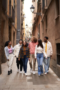 Vertical photo of young happy people walking in the street of the city. Smiling students laughing and having fun togethers. High quality photo