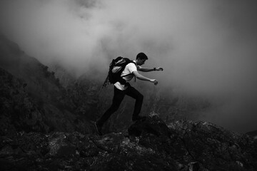 Montañero con una mochila saltando sobre unas piedras entre la niebla, Ruta del Cares, Asturias,...