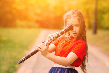 Young attractive girl playing clarinet, ebony in fall park
