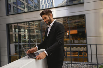 Smiling entrepreneur working on laptop standing on office terrace during working day