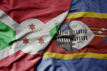big waving national colorful flag of eswatini and national flag of burundi .