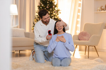 Making proposal. Man with engagement ring surprising his girlfriend at home on Christmas - obrazy, fototapety, plakaty