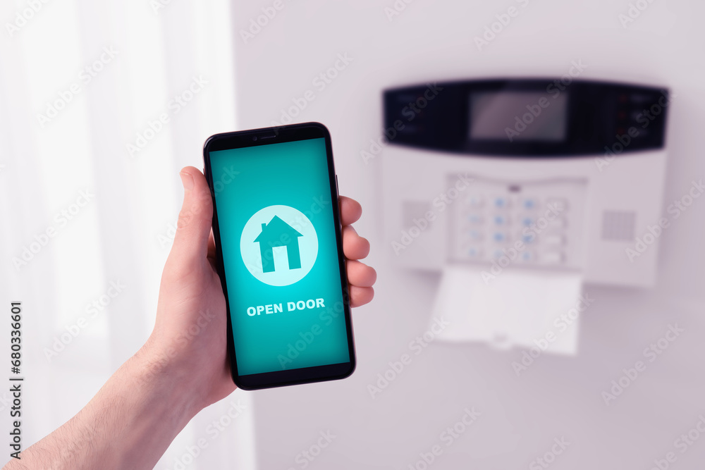 Poster man operating home alarm system via mobile phone against white wall with security control panel, clo