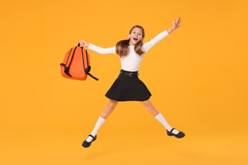 Fototapeta na wymiar Happy schoolgirl with backpack jumping on orange background