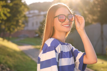 Beautiful smiling woman wearing sunglasses in park, space for text