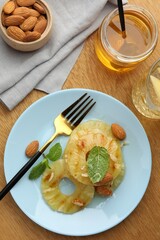 Tasty grilled pineapple slices served with mint and almonds on wooden table, flat lay
