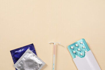Contraception choice. Pills, condoms and intrauterine device on beige background, flat lay. Space for text