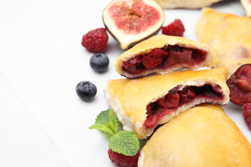 Delicious samosas, berries, mint leaves and fig on white tiled table, closeup. Space for text