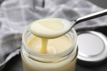 Condensed milk flowing down from spoon into jar on table, closeup