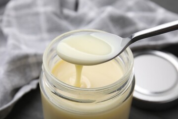 Condensed milk flowing down from spoon into jar on table, closeup