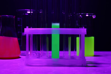 Laboratory glassware with luminous liquids on table against dark background