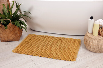 Soft bath mat, green plant and cosmetic products in bathroom