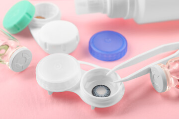Cases with color contact lenses and tweezers on pink background